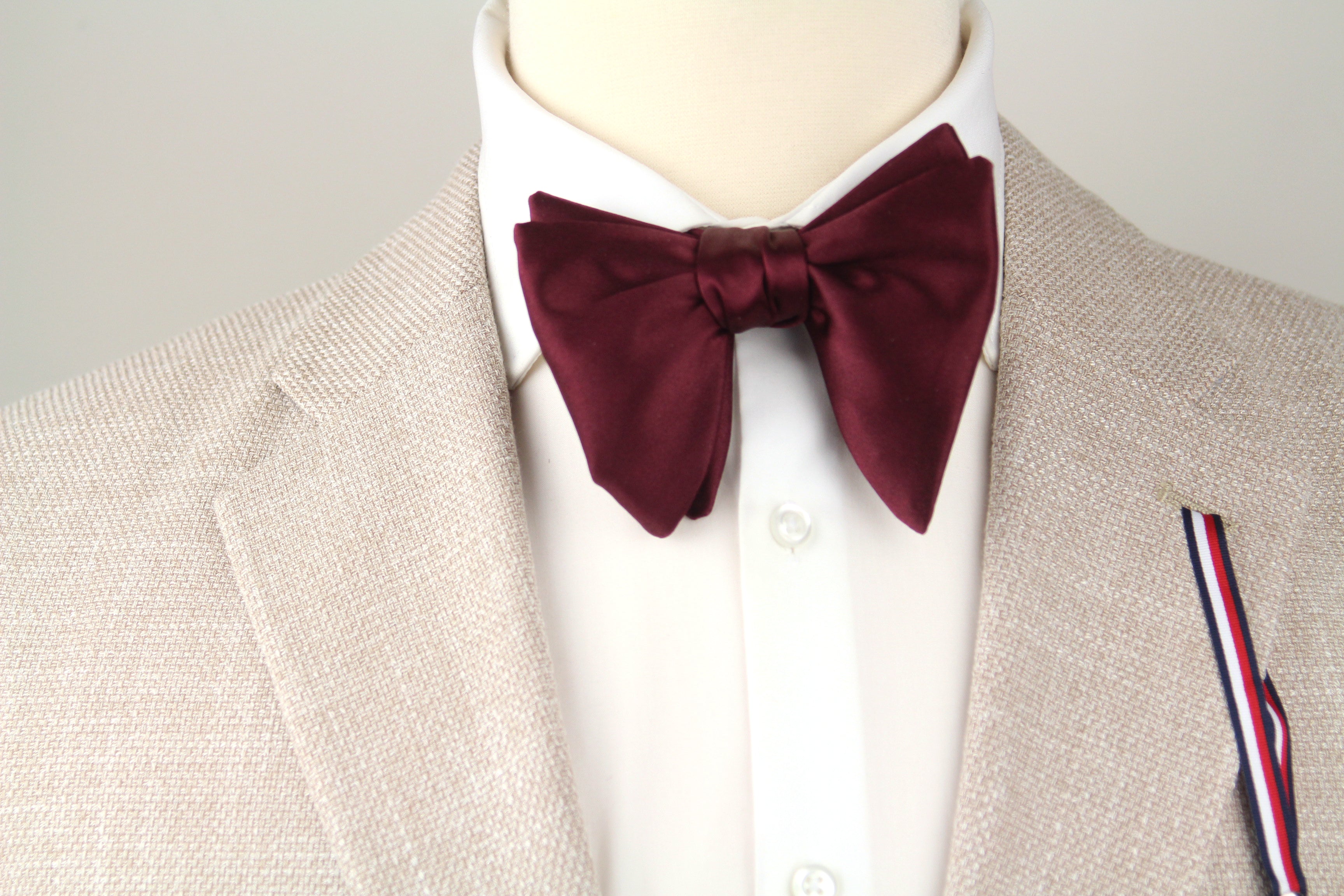 Mannequin wearing a beige suit with a white shirt and burgundy bow tie.