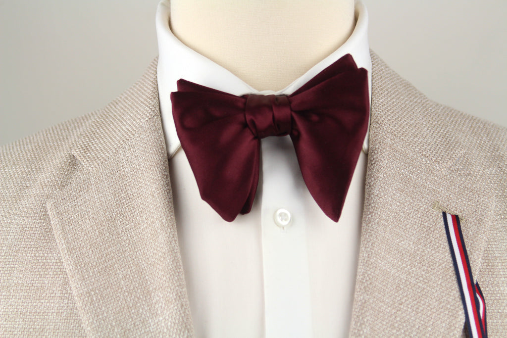 Mannequin wearing a beige blazer, white shirt, and burgundy bow tie on a light gray background