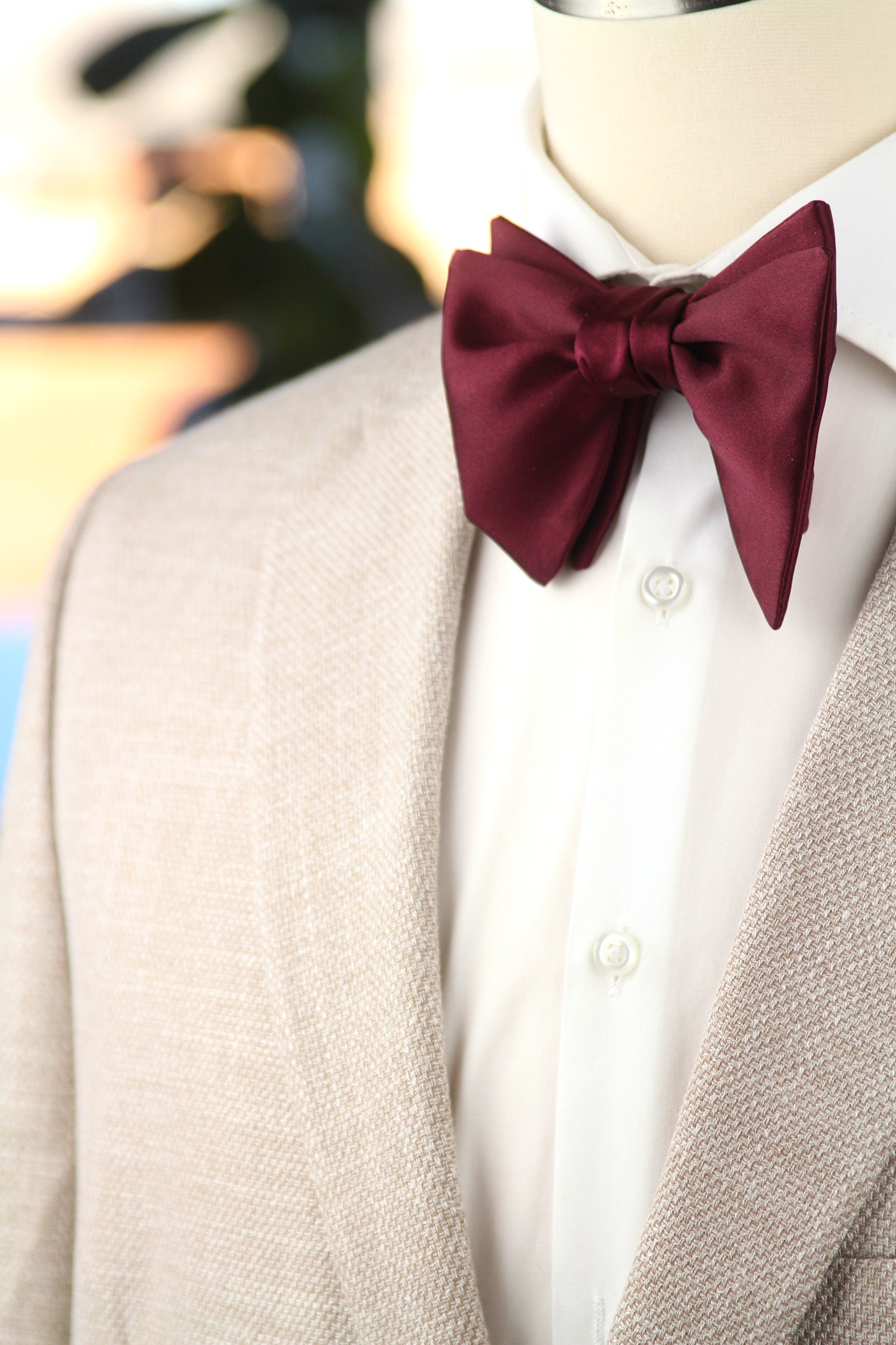Mannequin wearing a beige suit with a white shirt and burgundy bow tie.