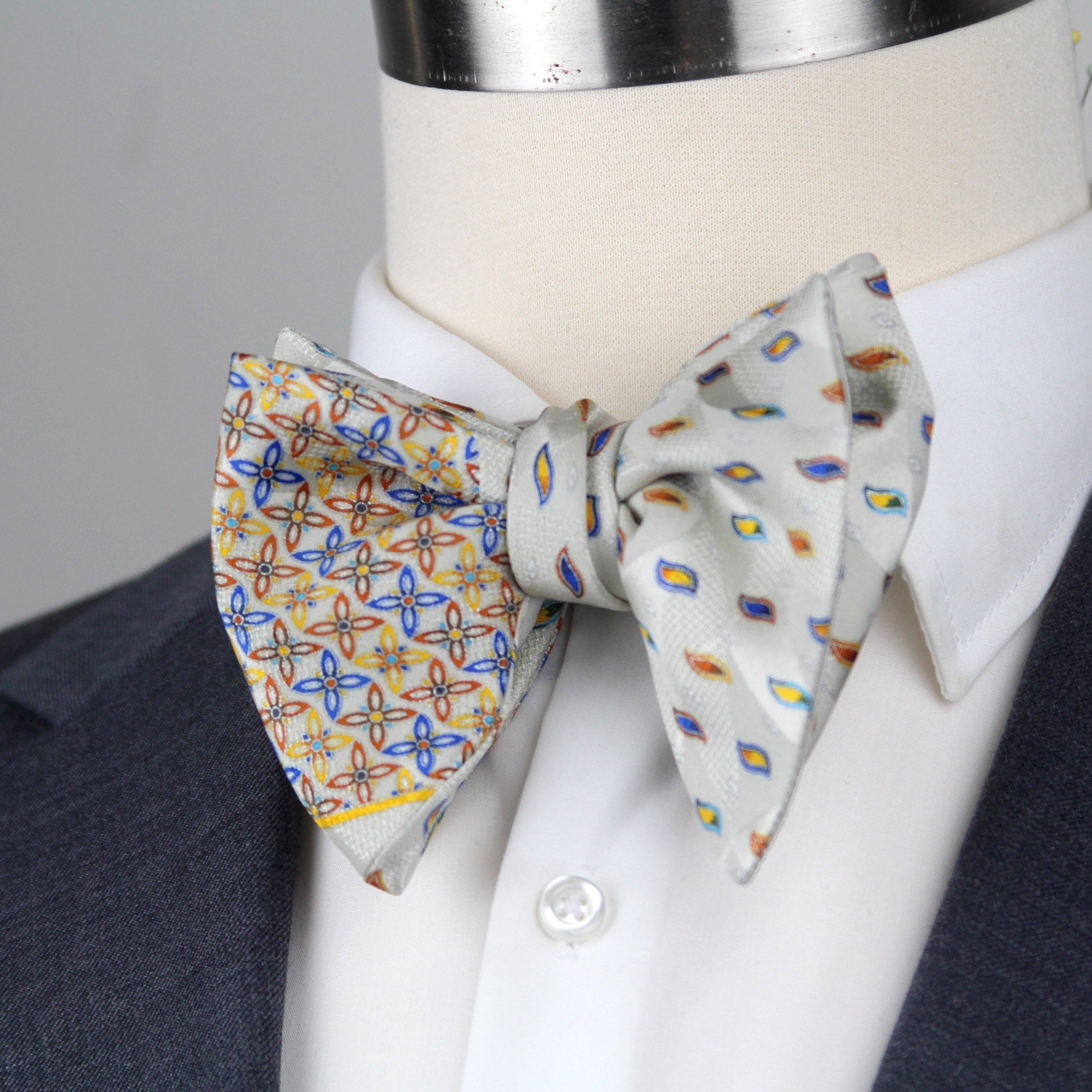 Two patterned bow ties on a mannequin with a suit jacket.
