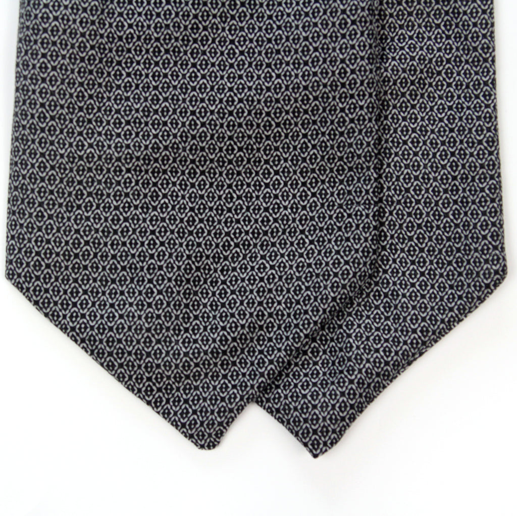 A close-up of a necktie with a dark navy blue base and a repeating small white geometric pattern, folded over on a plain white background.