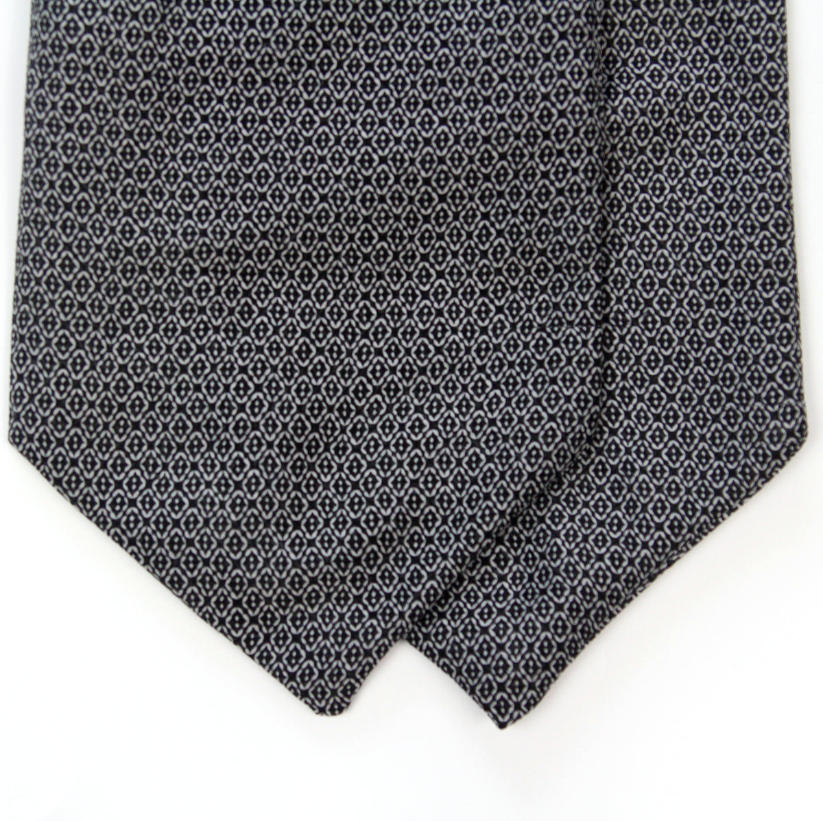 A close-up of a necktie with a dark navy blue base and a repeating small white geometric pattern, folded over on a plain white background.