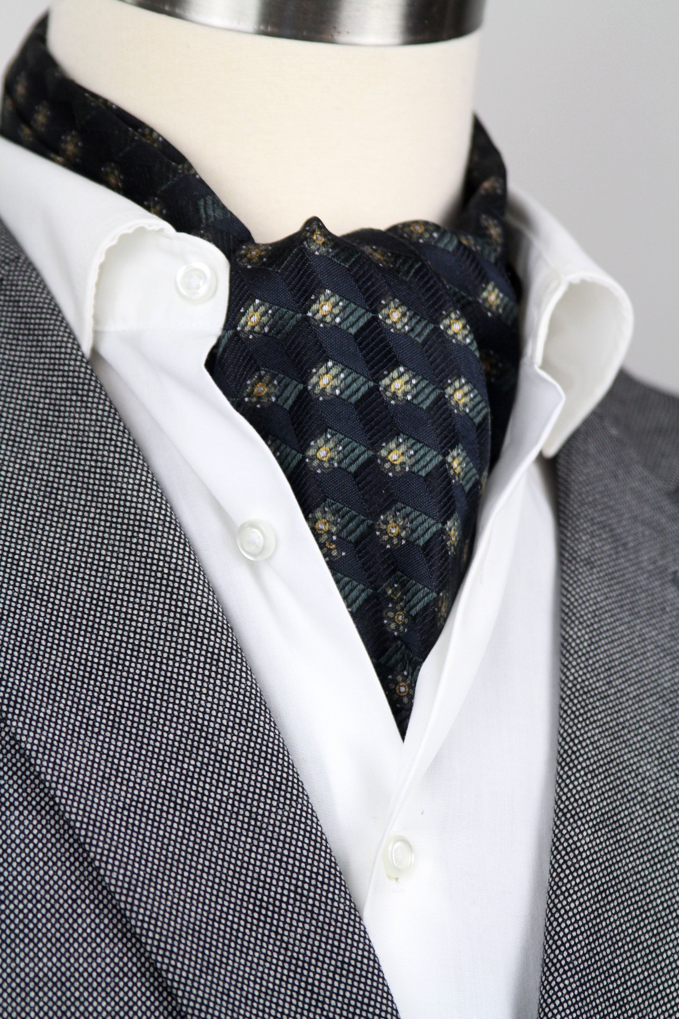 Mannequin wearing a gray suit with a white shirt and patterned cravat.