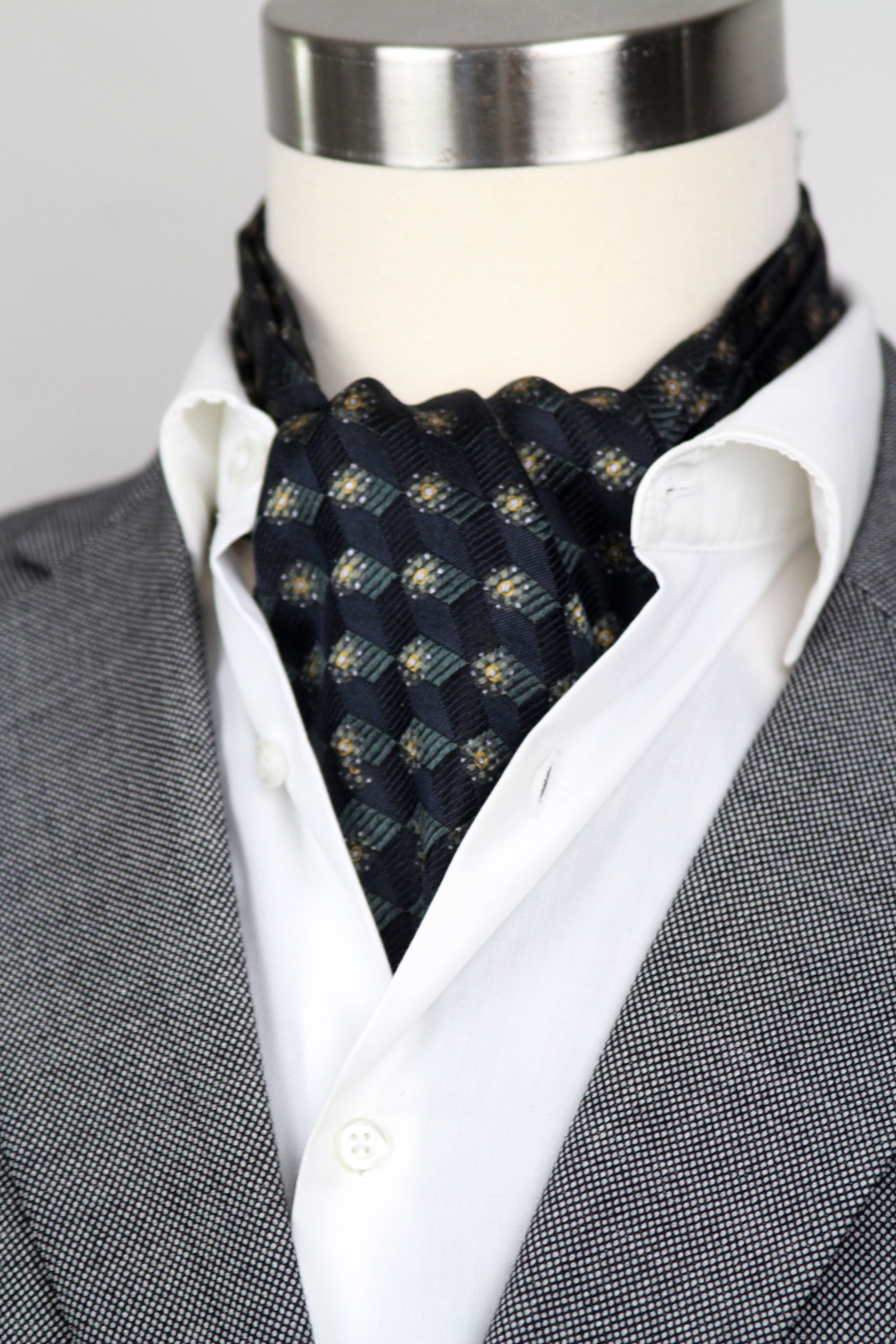 Mannequin wearing a gray suit with a white shirt and black patterned cravat.