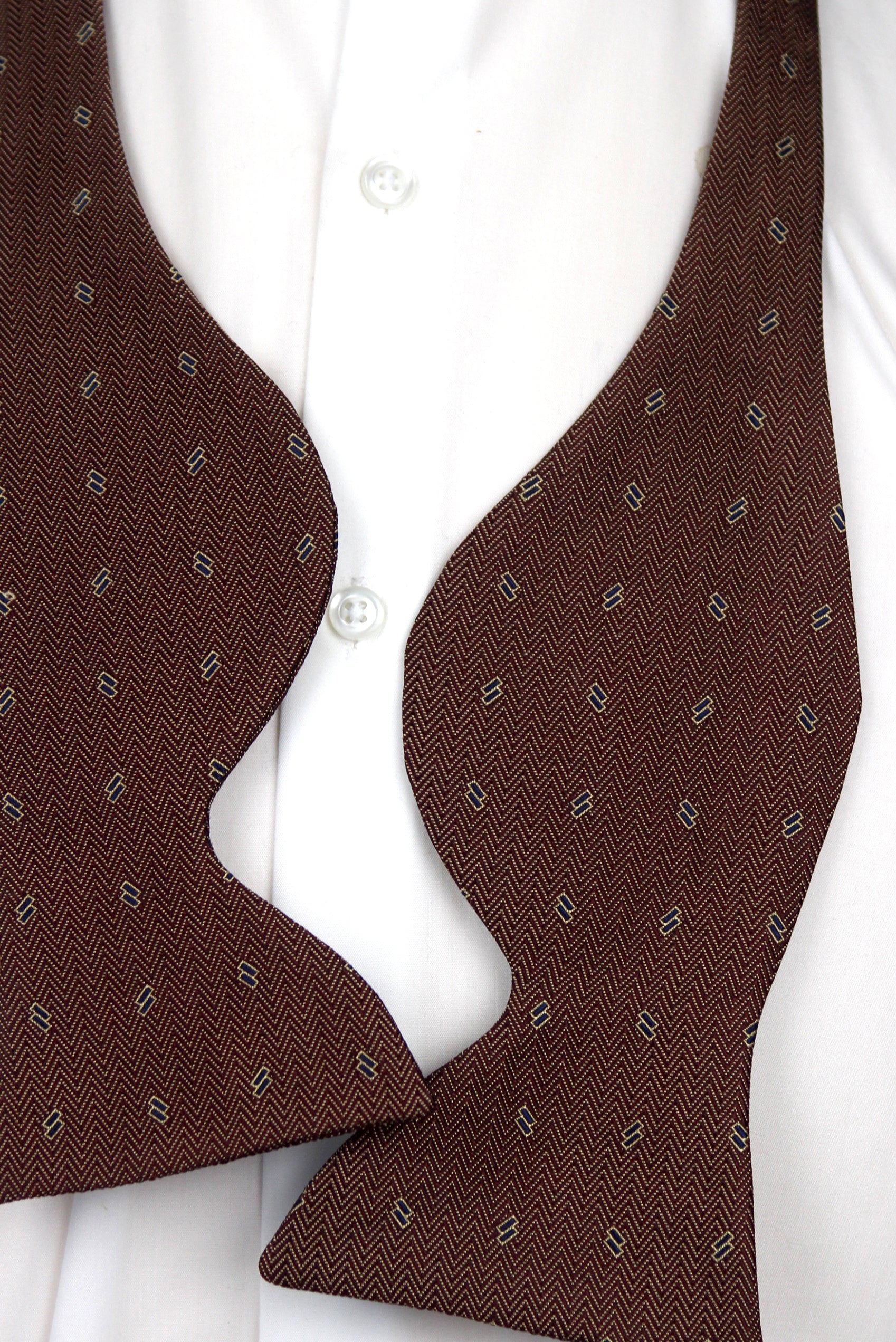 A close-up of a brown herringbone patterned bow tie worn over a white dress shirt.