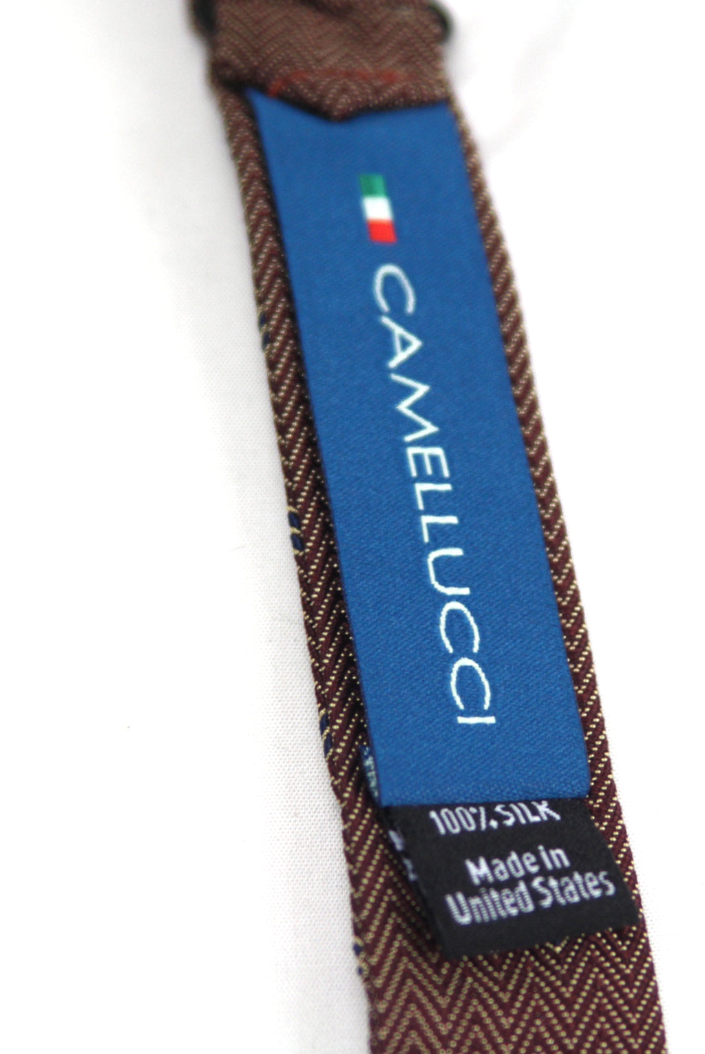 Close-up of a Camelucci silk necktie showing the blue brand label with white text and a black '100% Silk Made in United States' tag, on a white background.