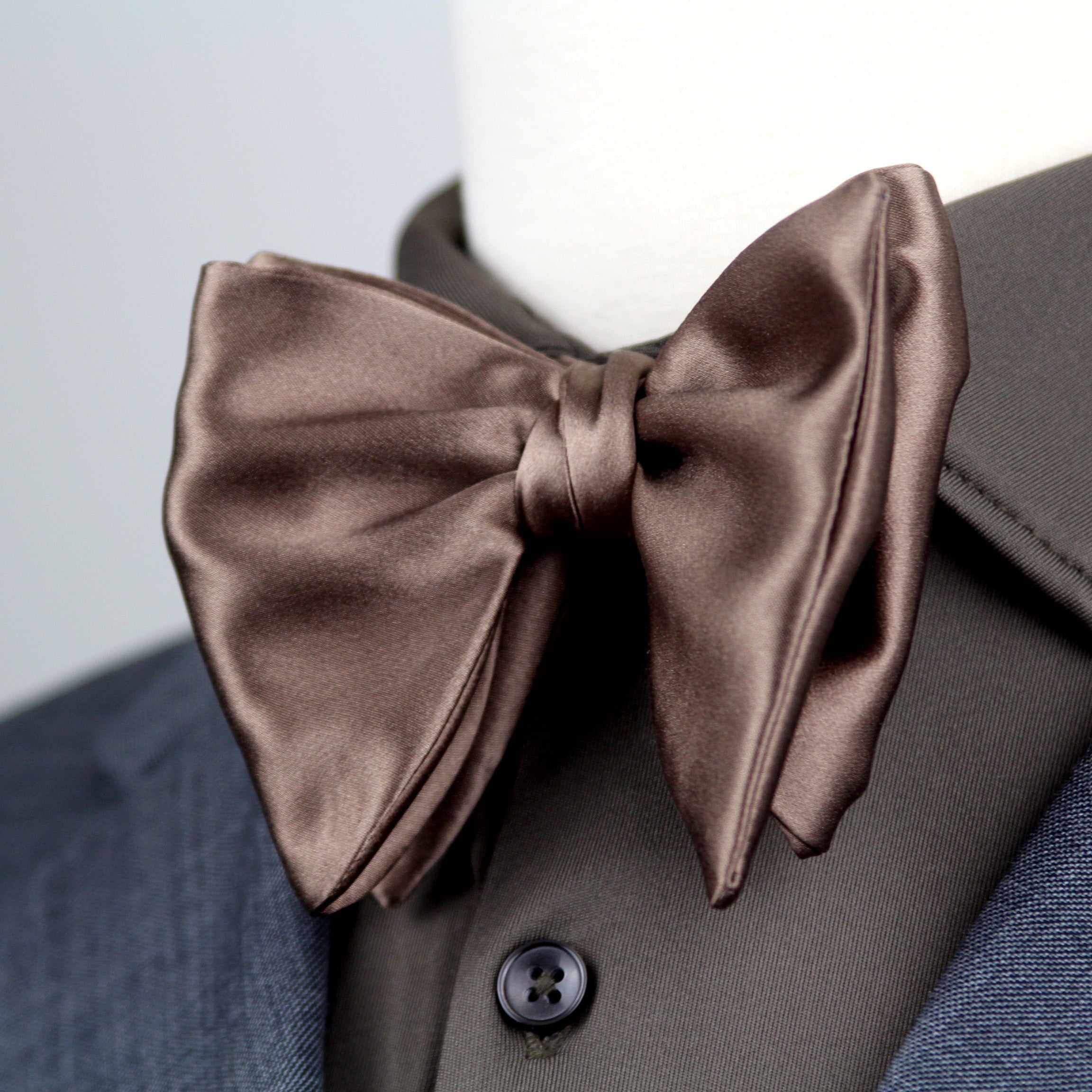 Brown satin bow tie on a mannequin with a gray suit jacket.