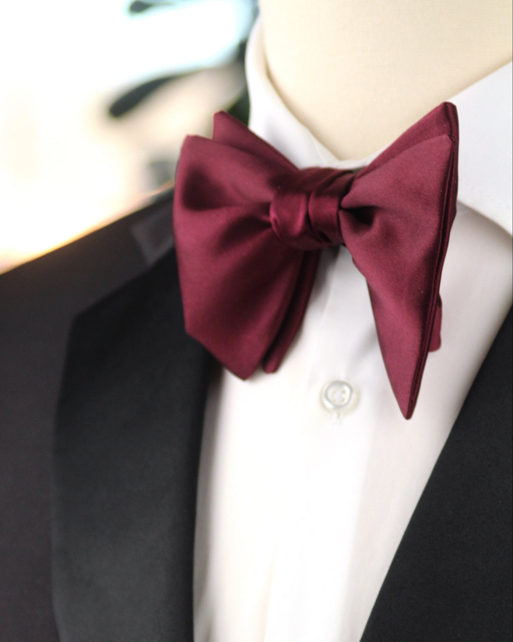Mannequin wearing a black tuxedo with a white shirt and burgundy bow tie.