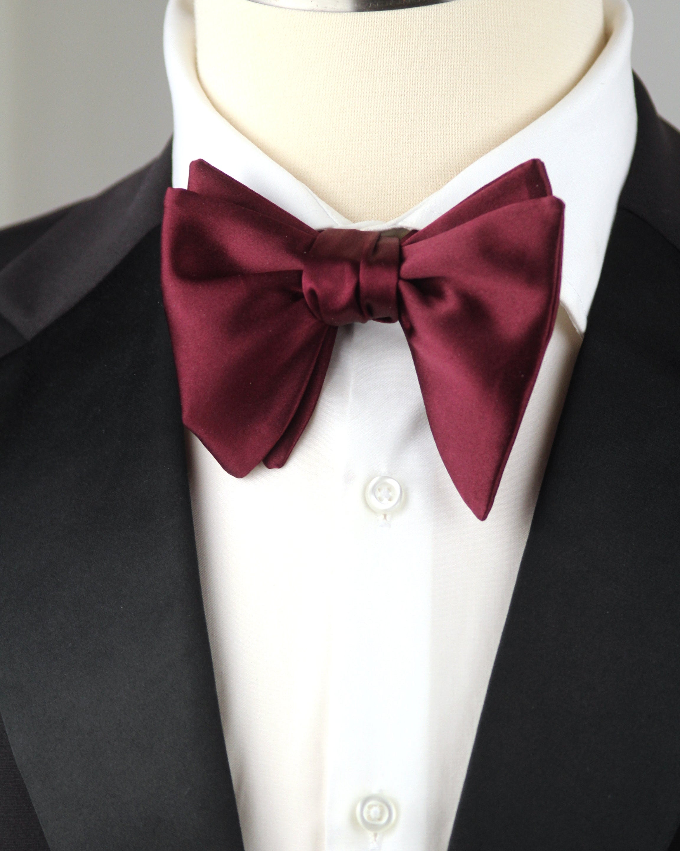 Burgundy bow tie on a mannequin wearing a white shirt and black jacket.