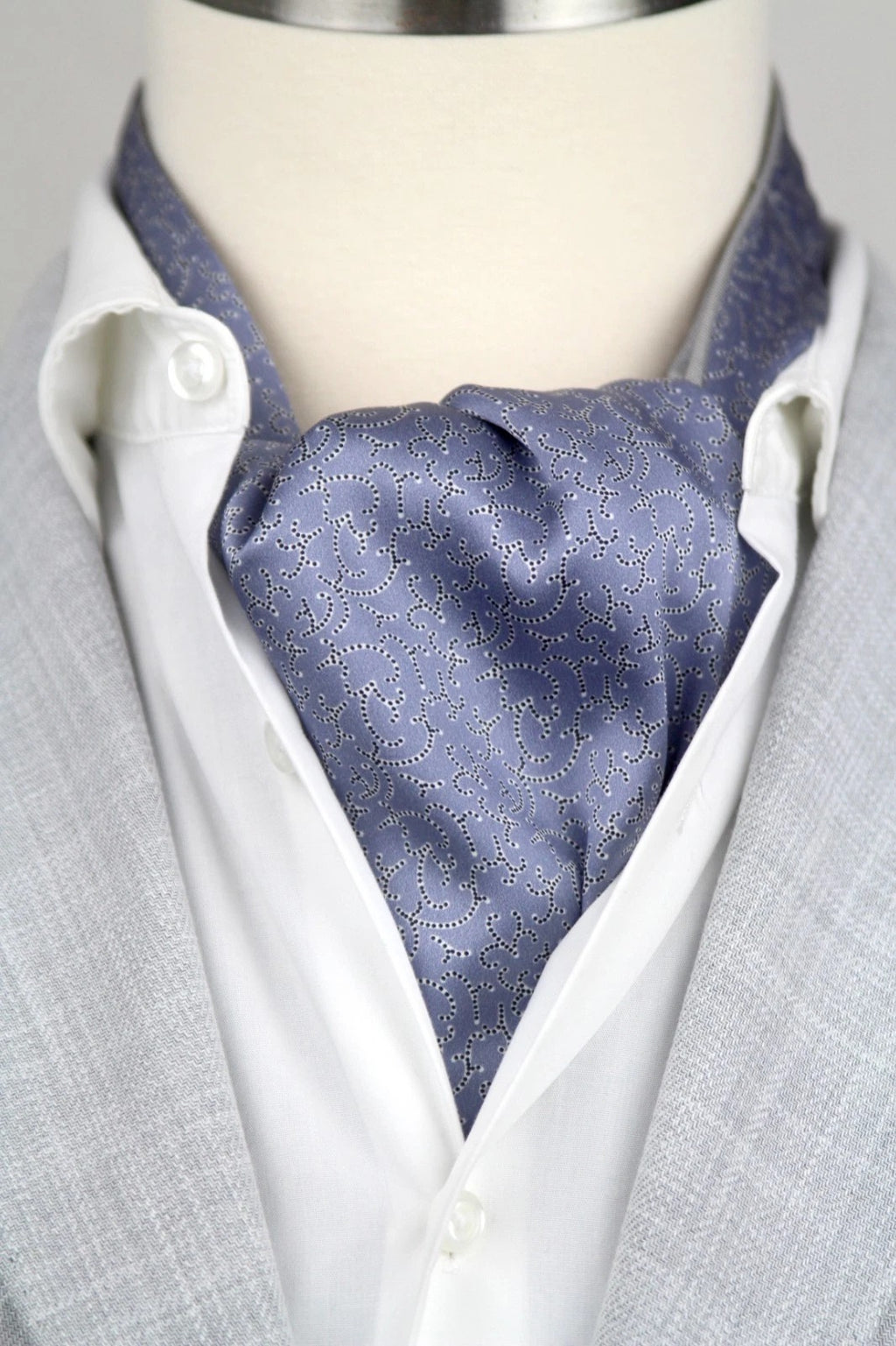 Mannequin wearing a light gray suit with a white shirt and blue patterned cravat.