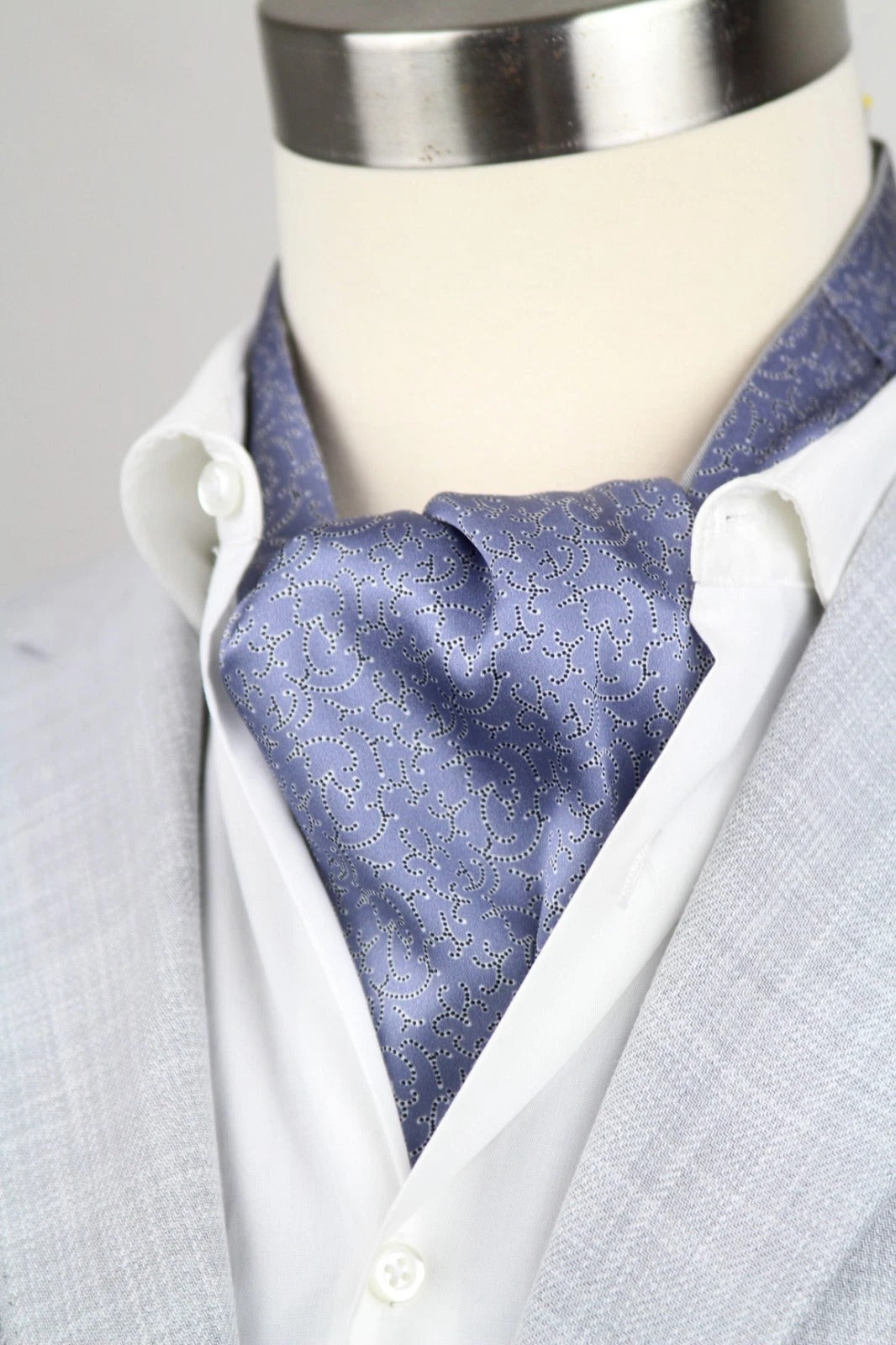 Mannequin wearing a light gray suit with a white shirt and blue patterned cravat.