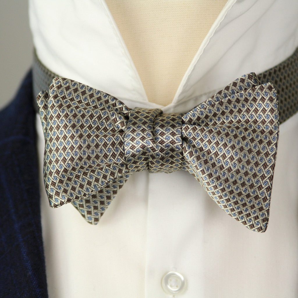 Silver patterned bow tie on a white shirt with a dark suit jacket.