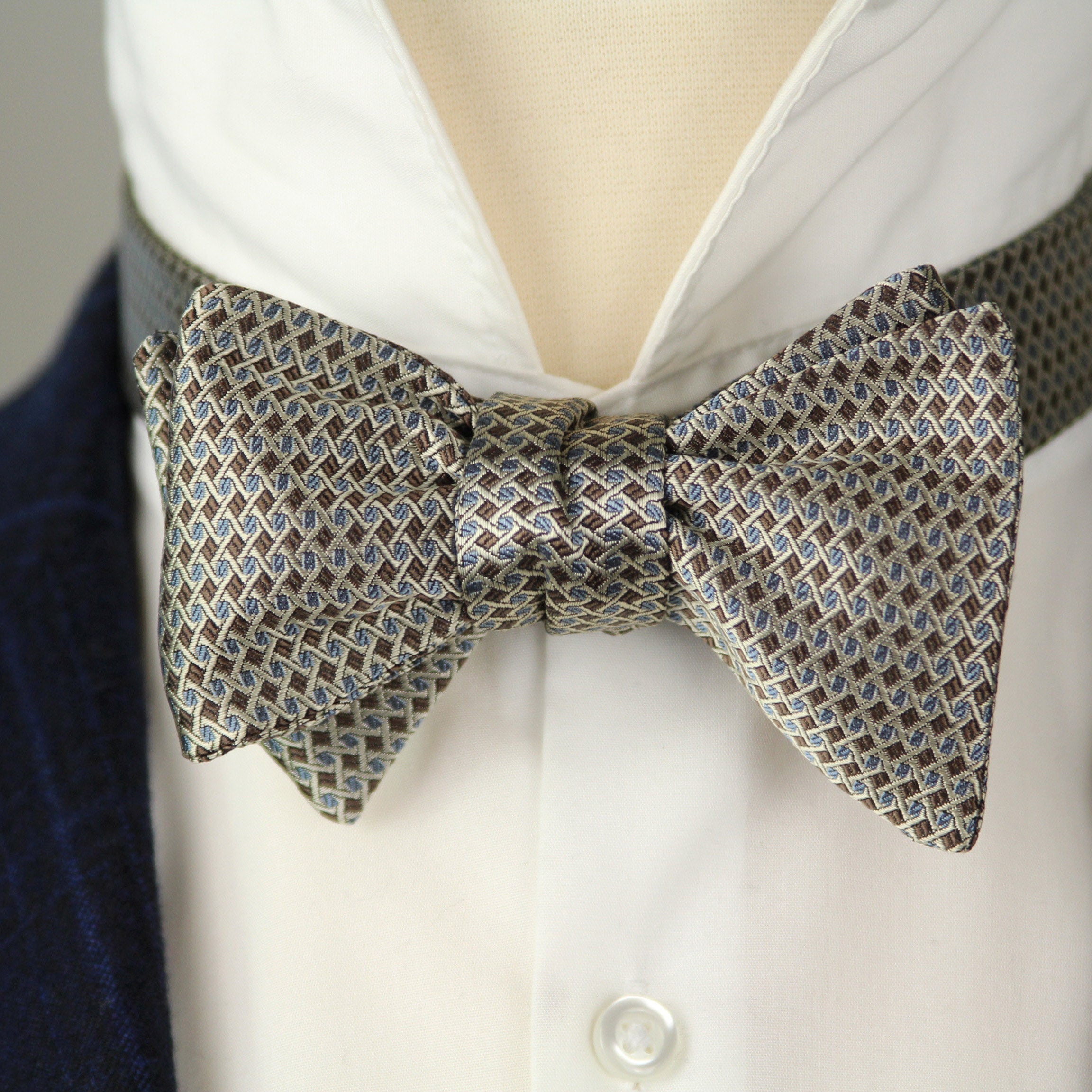 Silver patterned bow tie on a white shirt with a dark suit jacket.