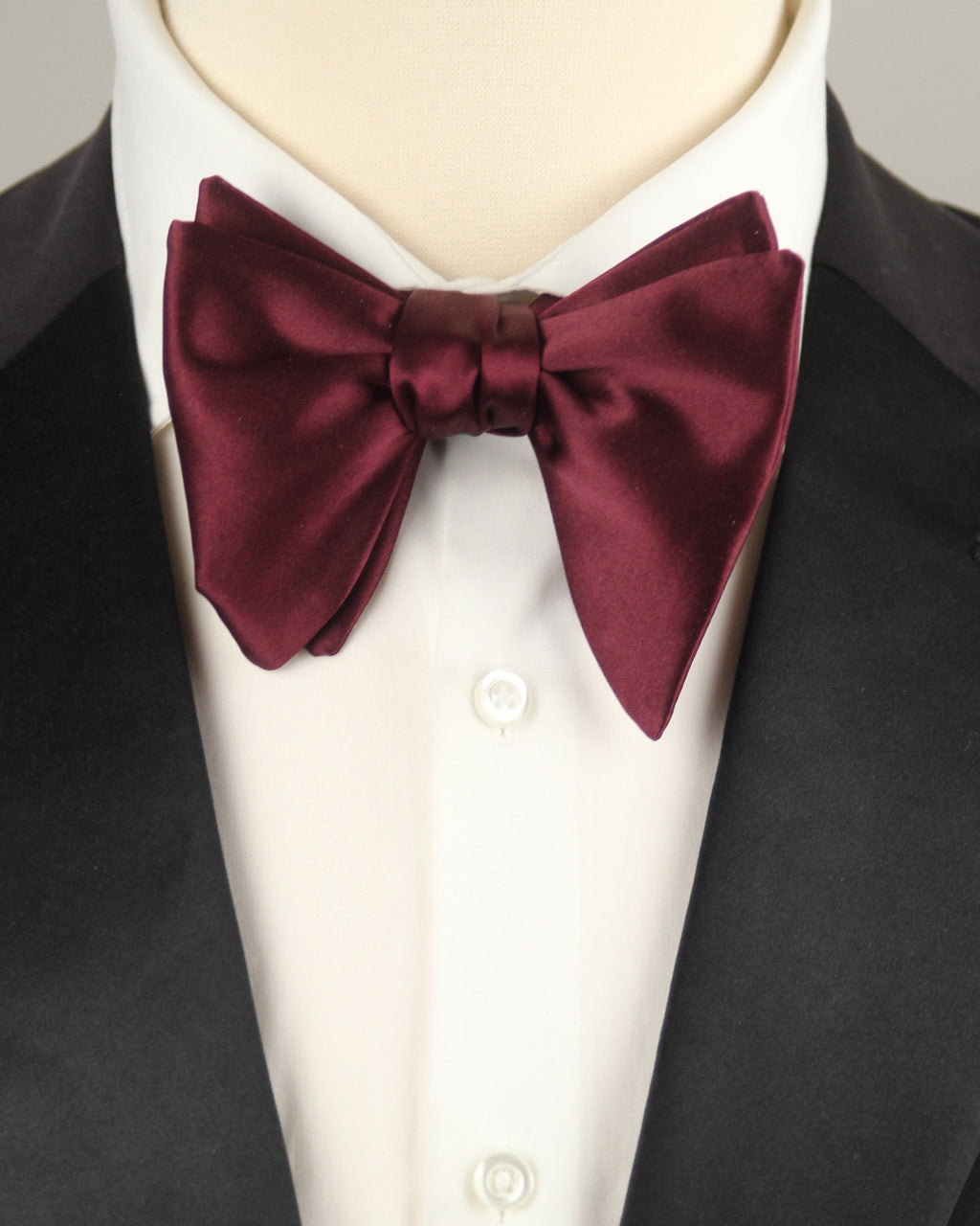 Maroon bow tie on a mannequin wearing a black tuxedo and white shirt.