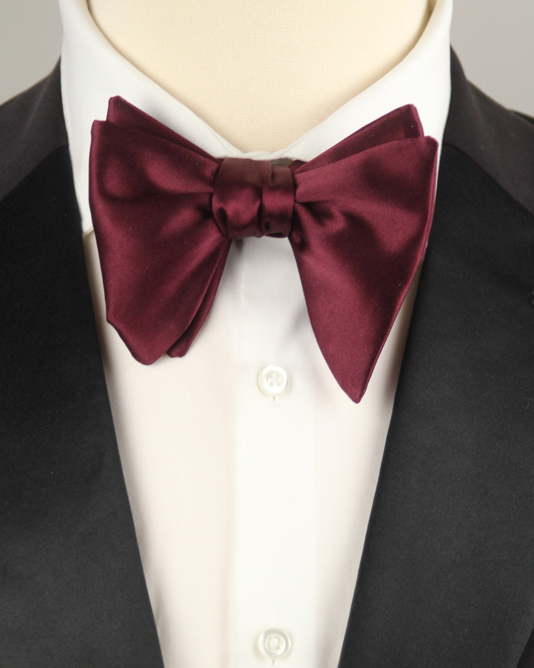Maroon bow tie on a mannequin wearing a black tuxedo and white shirt.