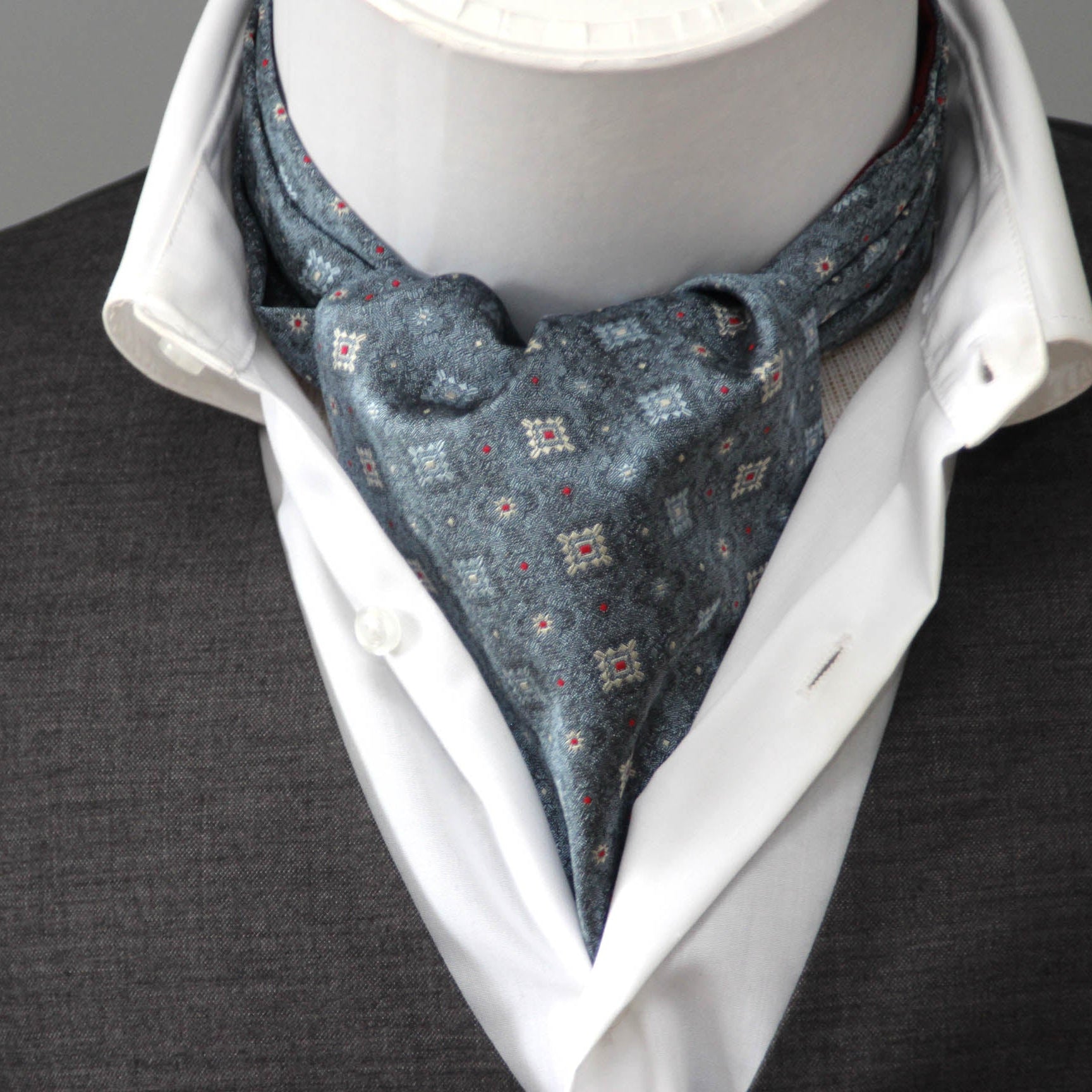 Mannequin wearing a white shirt, gray vest, and patterned cravat against a neutral background