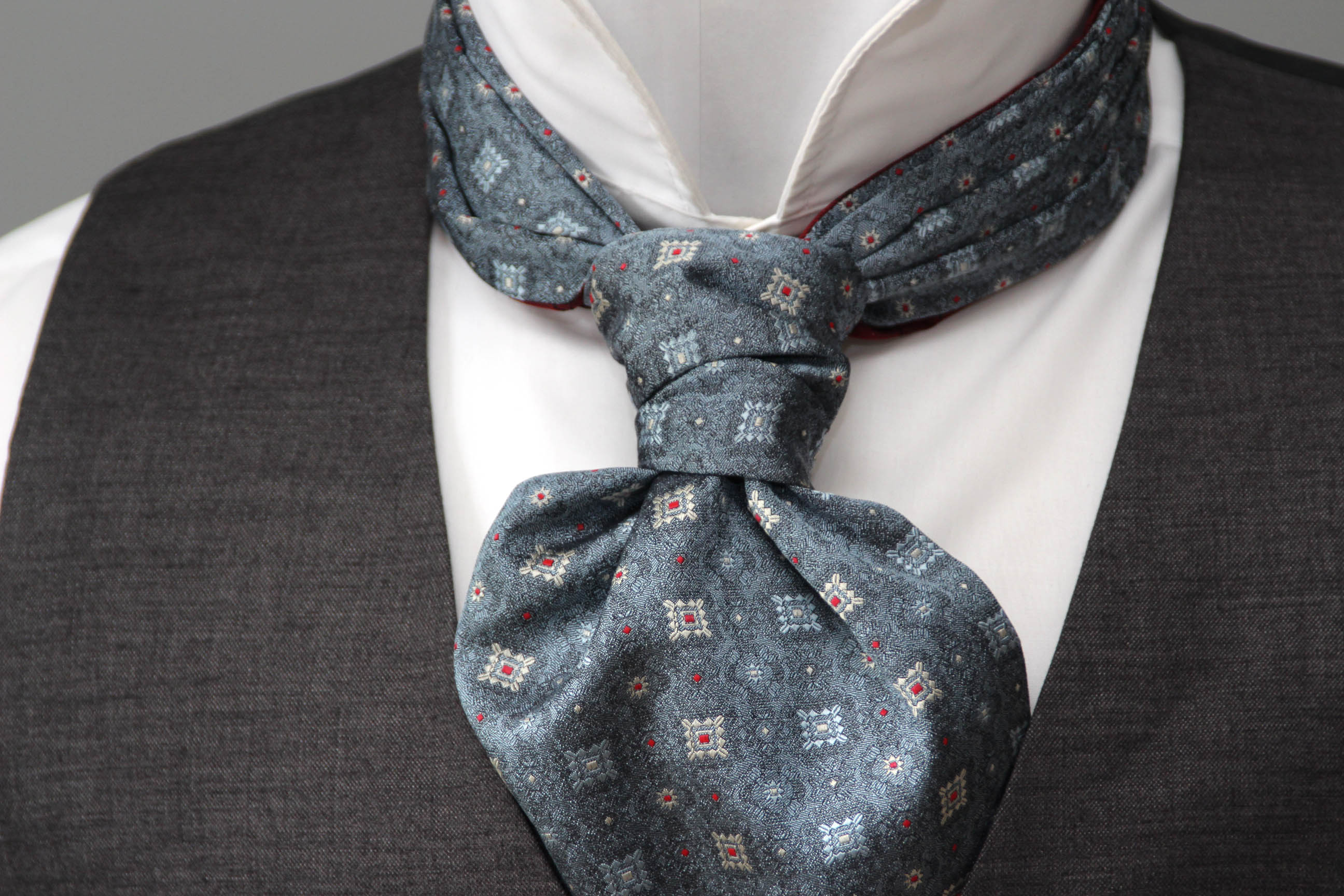 Mannequin wearing a gray patterned cravat with a gray vest and white shirt.