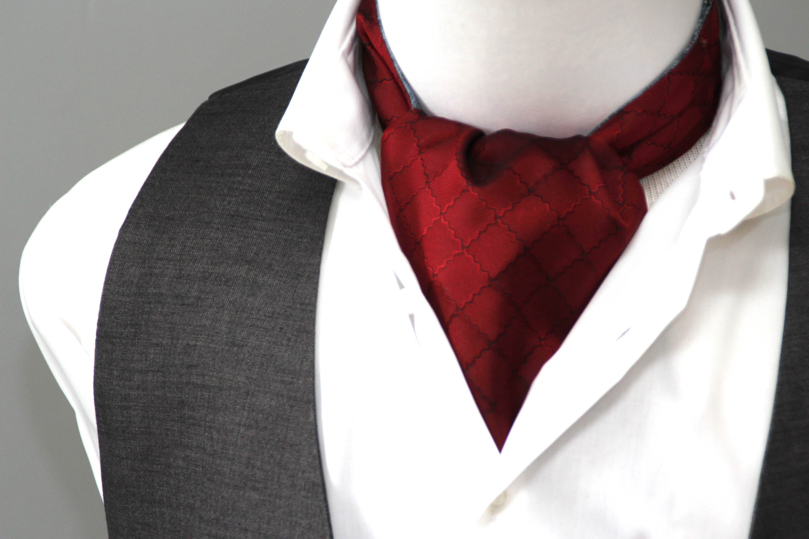 Mannequin wearing a white shirt, gray vest, and red cravat against a gray background