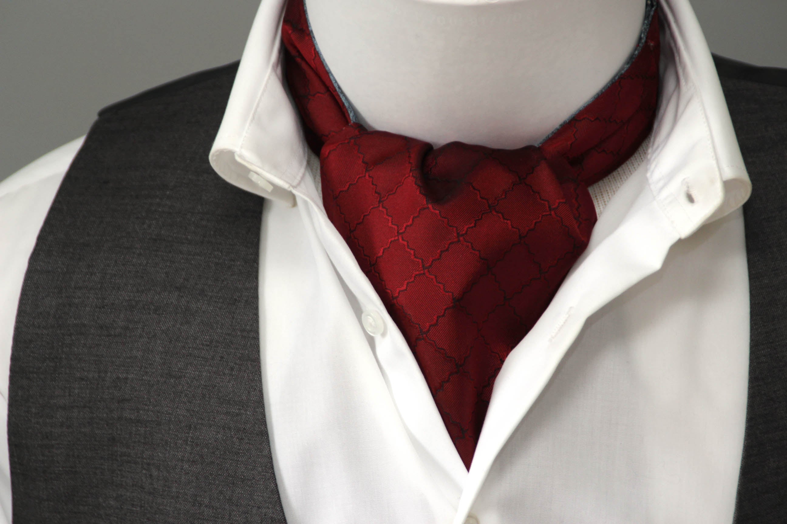 Red cravat on a mannequin with a white shirt and gray vest.