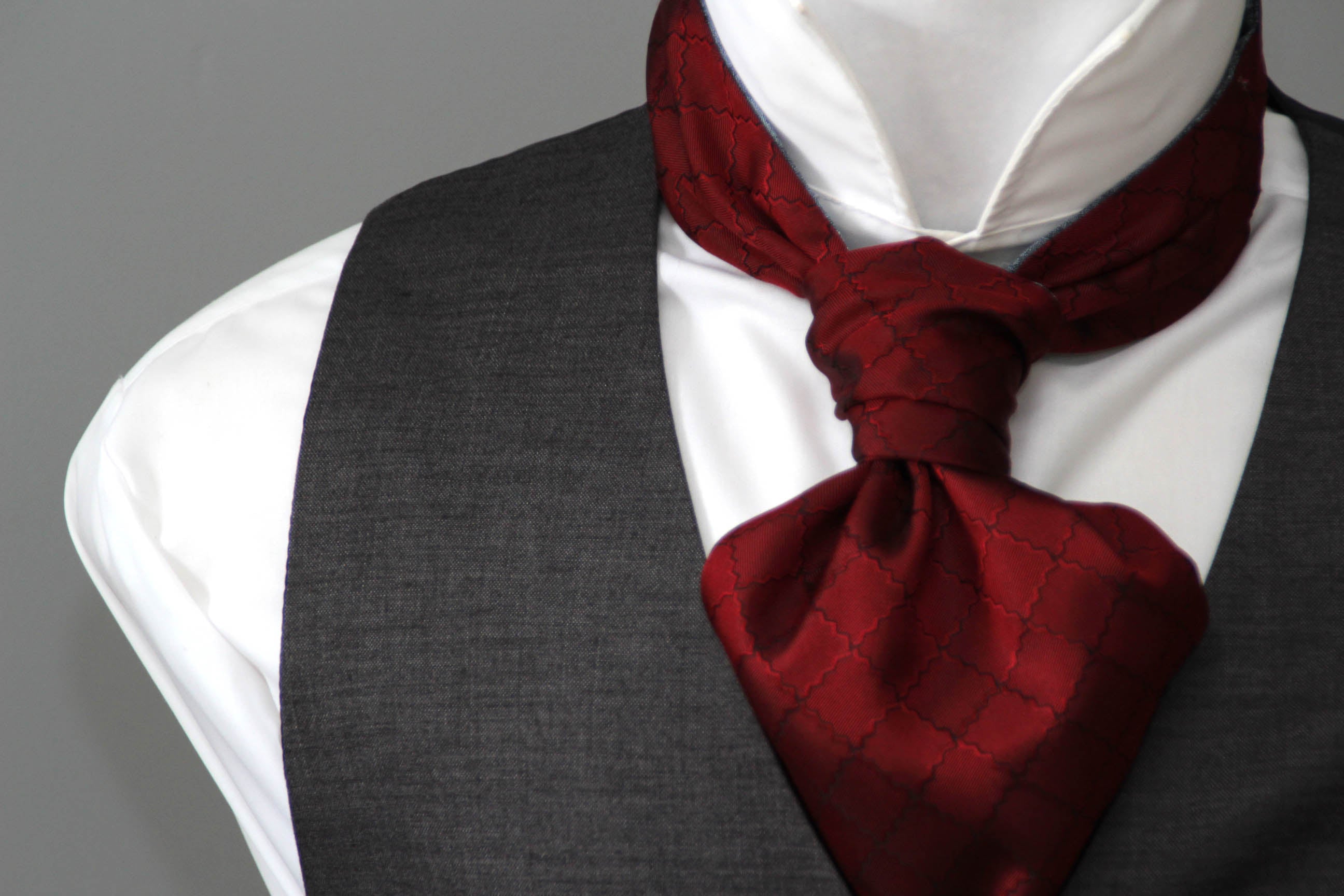 Mannequin wearing a white shirt, gray vest, and red scarf with a gray background