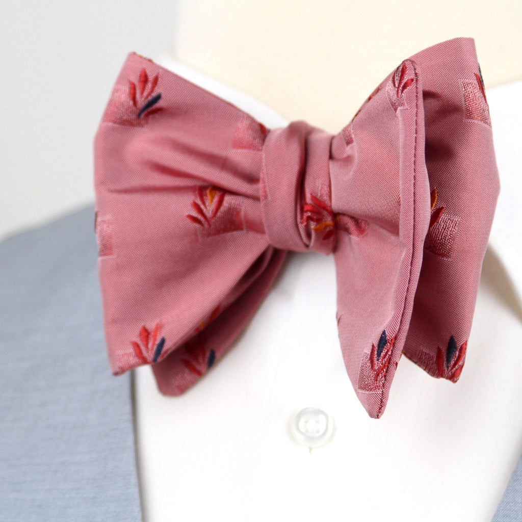 Pink bow tie with floral pattern on a mannequin wearing a gray suit and white shirt.