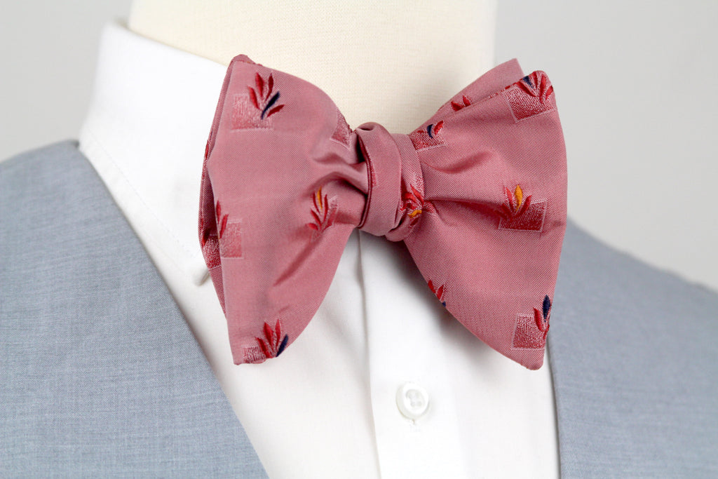 Pink bow tie with floral pattern on a mannequin wearing a gray suit and white shirt.