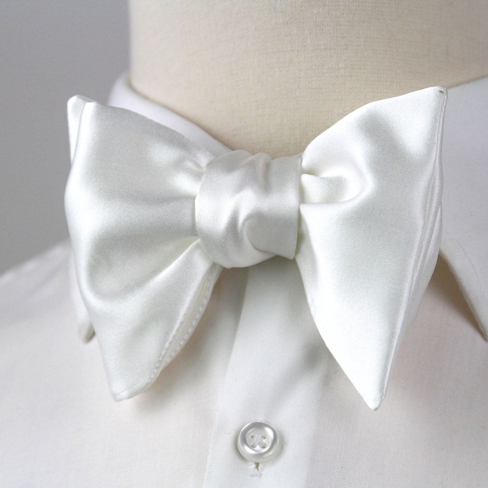 White bow tie on a mannequin wearing a white shirt with a gray background