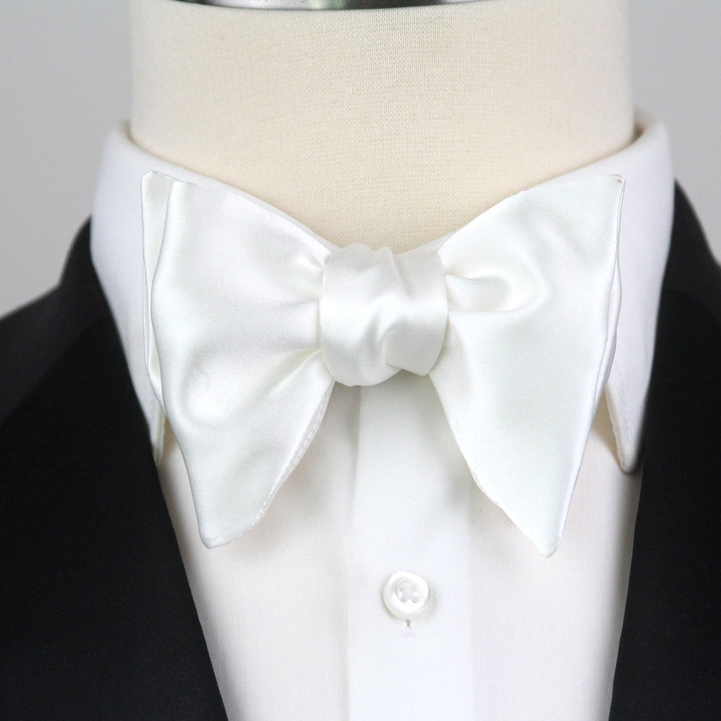 White bow tie on a mannequin with a black suit jacket against a gray background