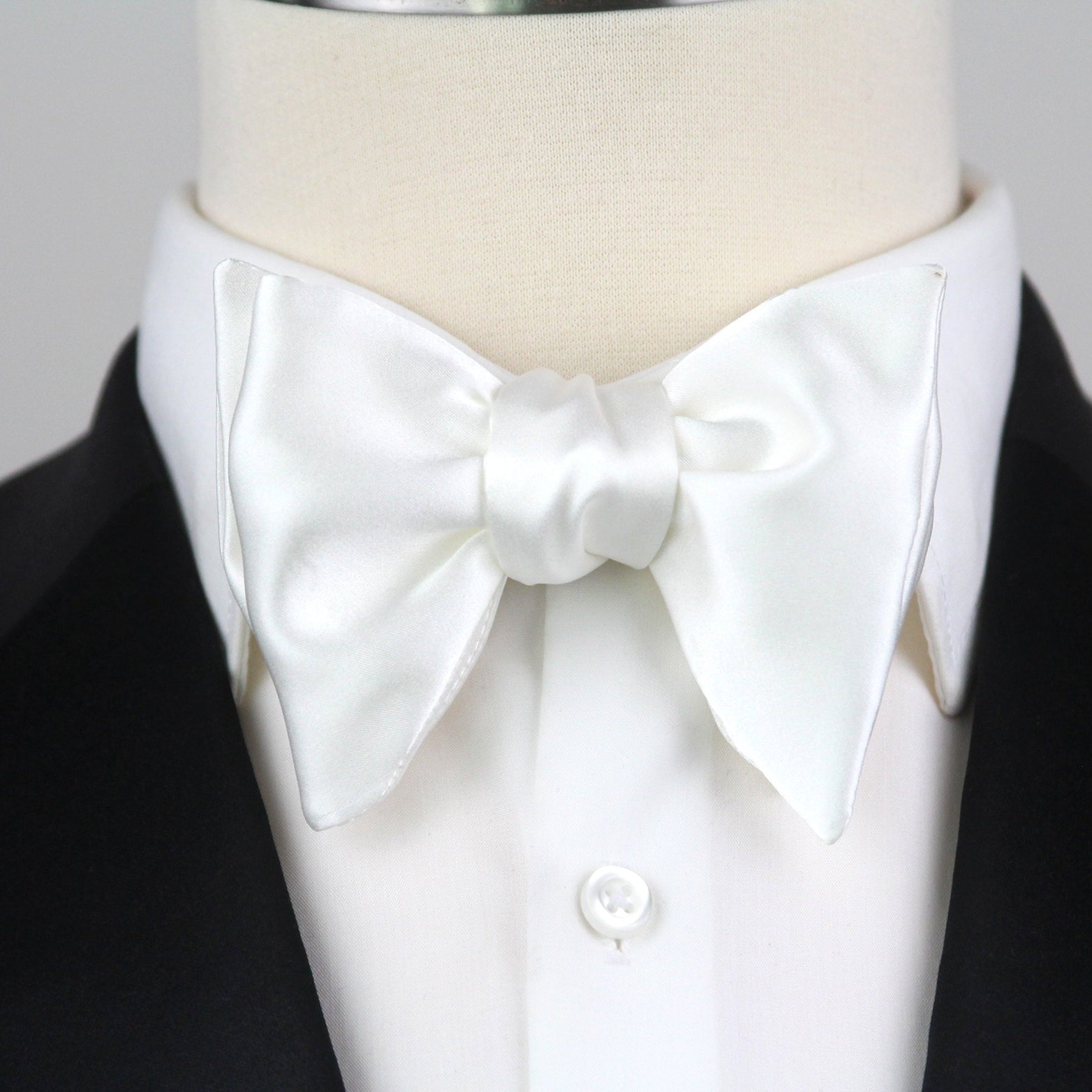 White bow tie on a mannequin with a black suit jacket against a gray background
