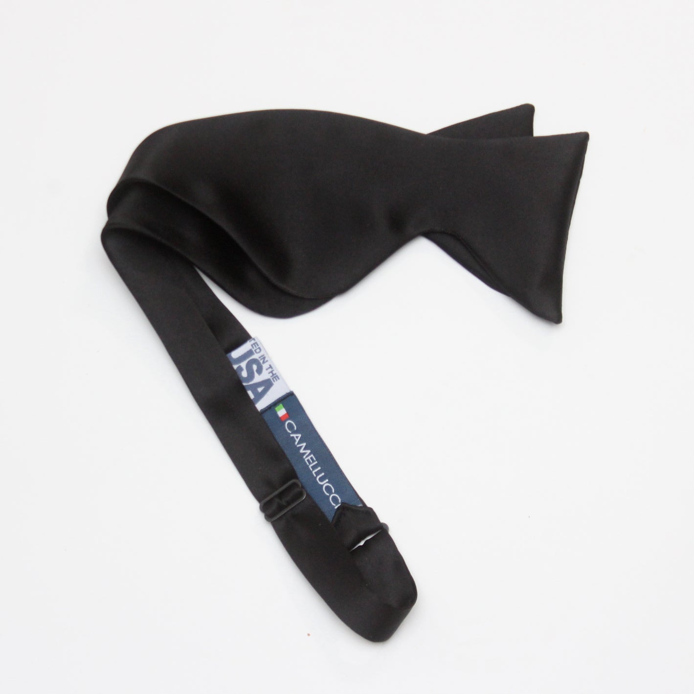 A large black silk bow tie tied around a white collar, with a smooth, satin finish and rounded ends.