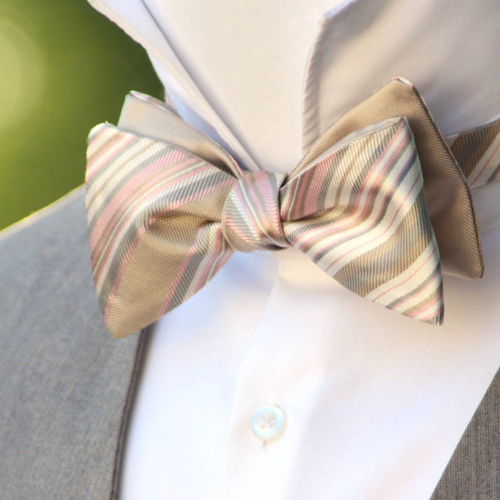 A close-up of a champagne stripe reversible self-tie bow tie tied on a mannequin dressed in a suit and white shirt.